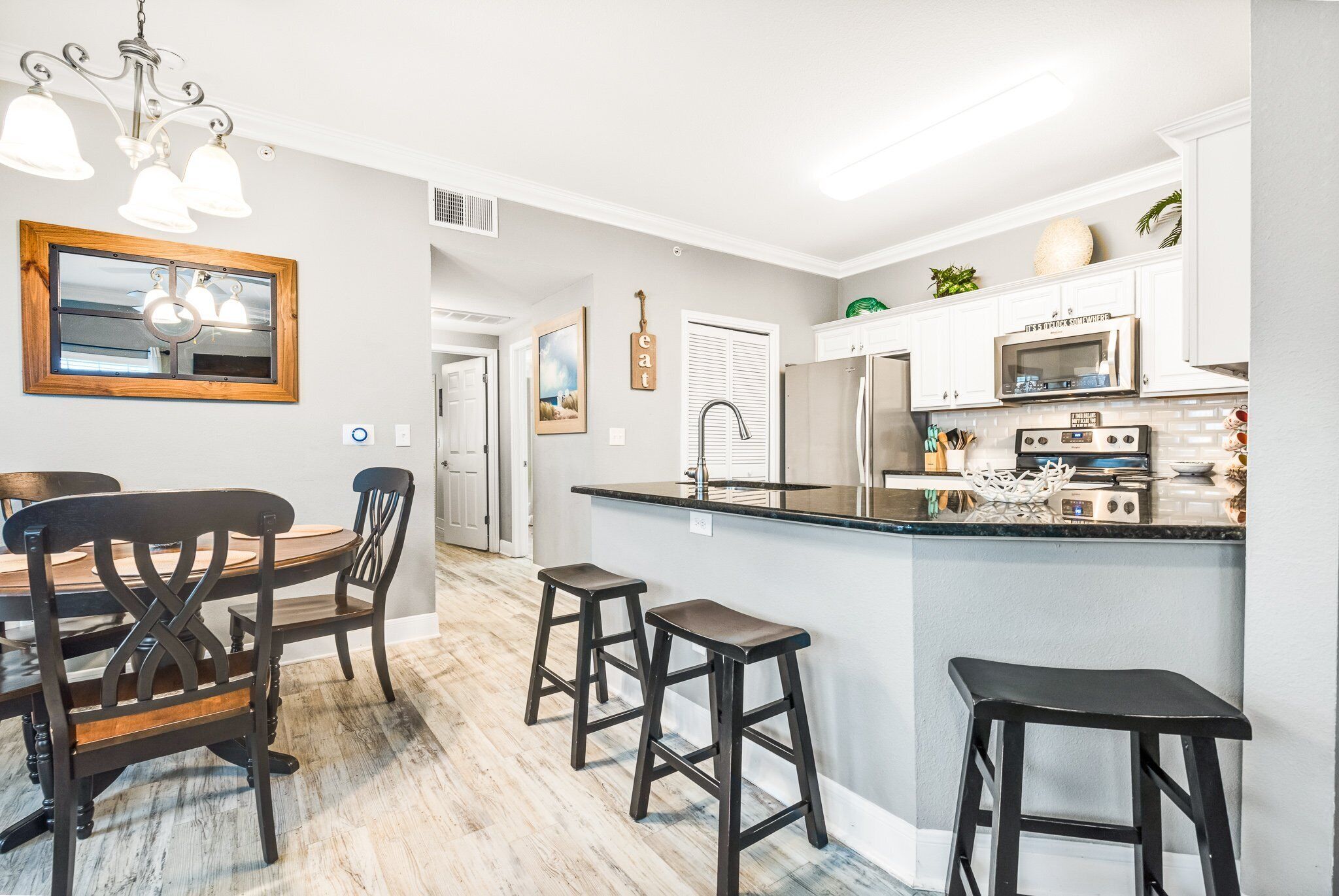 A kitchen with a wooden dining table, bar stools, a refrigerator, and a microwave.