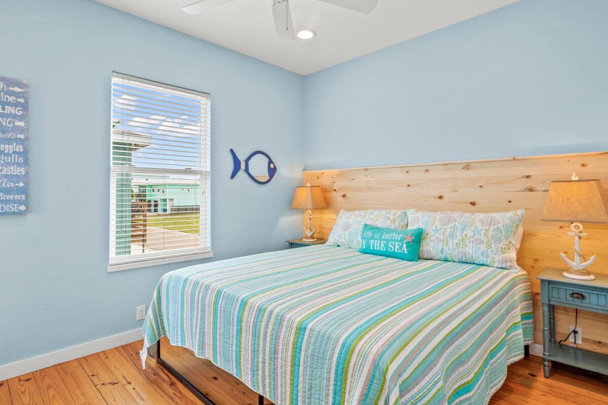 Une chambre à coucher comprenant un lit, une table de chevet, une lampe, une fenêtre avec des stores et un élément de décoration murale.