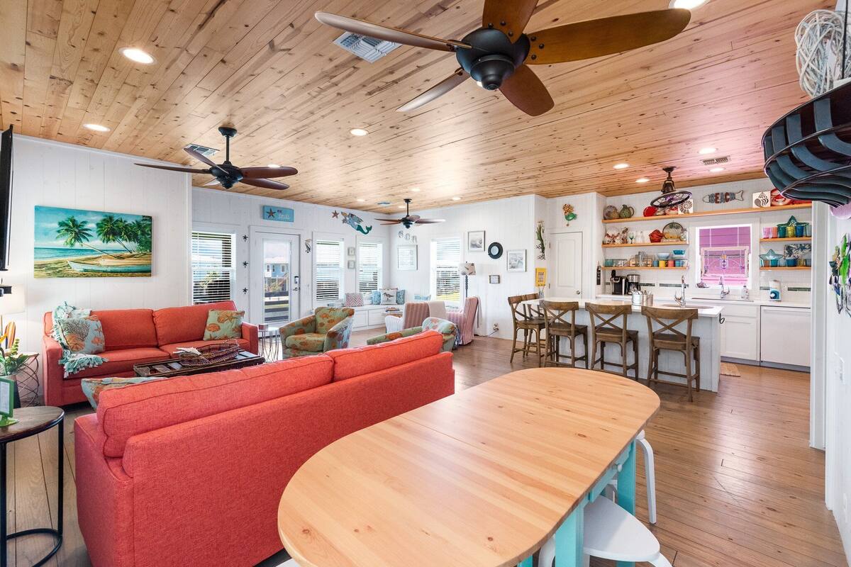 Un vaste espace de vie doté d’un plafond en bois, d’un canapé rouge, d’une table à manger en bois et d’un coin cuisine avec des meubles blancs et divers éléments de décoration.