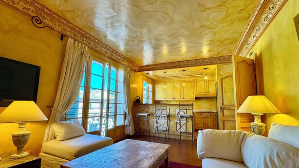 Una habitación con sofá, mesa de centro, televisión y una zona de cocina con armarios y mesa de comedor.