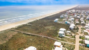 Luftaufnahme einer Küstenregion mit Strand, einem Steg und Wohngebäuden.