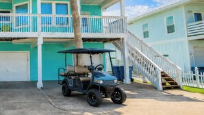A two-story building with a garage, a covered porch, and a staircase leading to a balcony. - Turquoise Treasure - Boardwalk to the Beach! Beach Gear Credit I (Port Aransas)