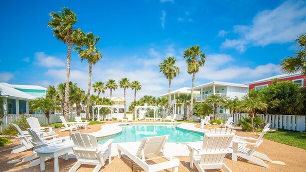 A pool area with white lounge chairs and palm trees. - Turquoise Treasure - Boardwalk to the Beach! Beach Gear Credit I (Port Aransas)