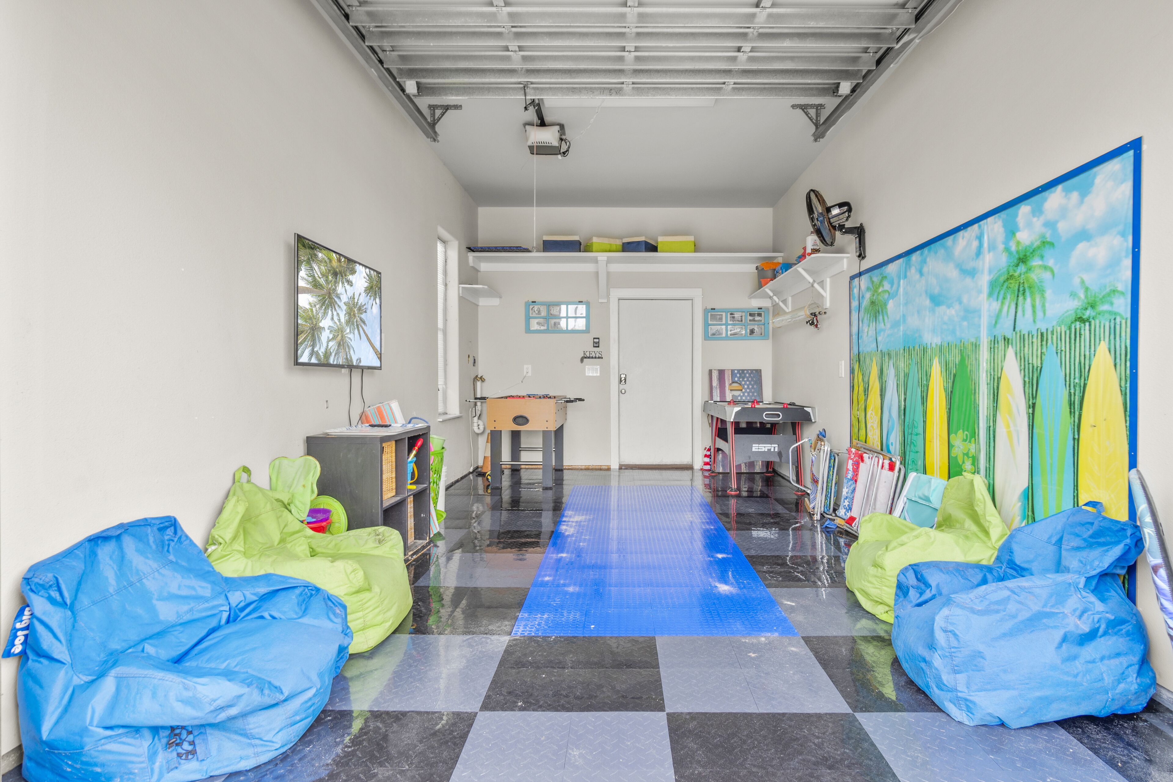 A hallway with a checkered floor, bean bags, a painting of palm trees, and a projector mounted on the ceiling.