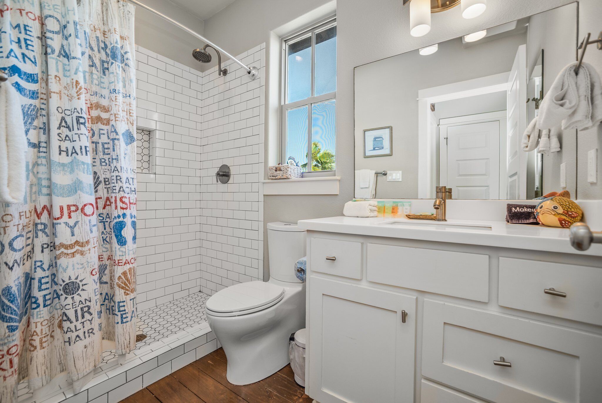 Ein Badezimmer mit Dusche, Toilette und Waschtisch mit Schubladen und Spiegel.
