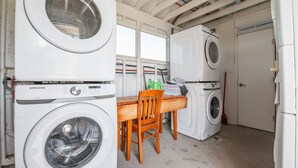 A laundry room with stacked washing machines, a wooden table, and a chair.