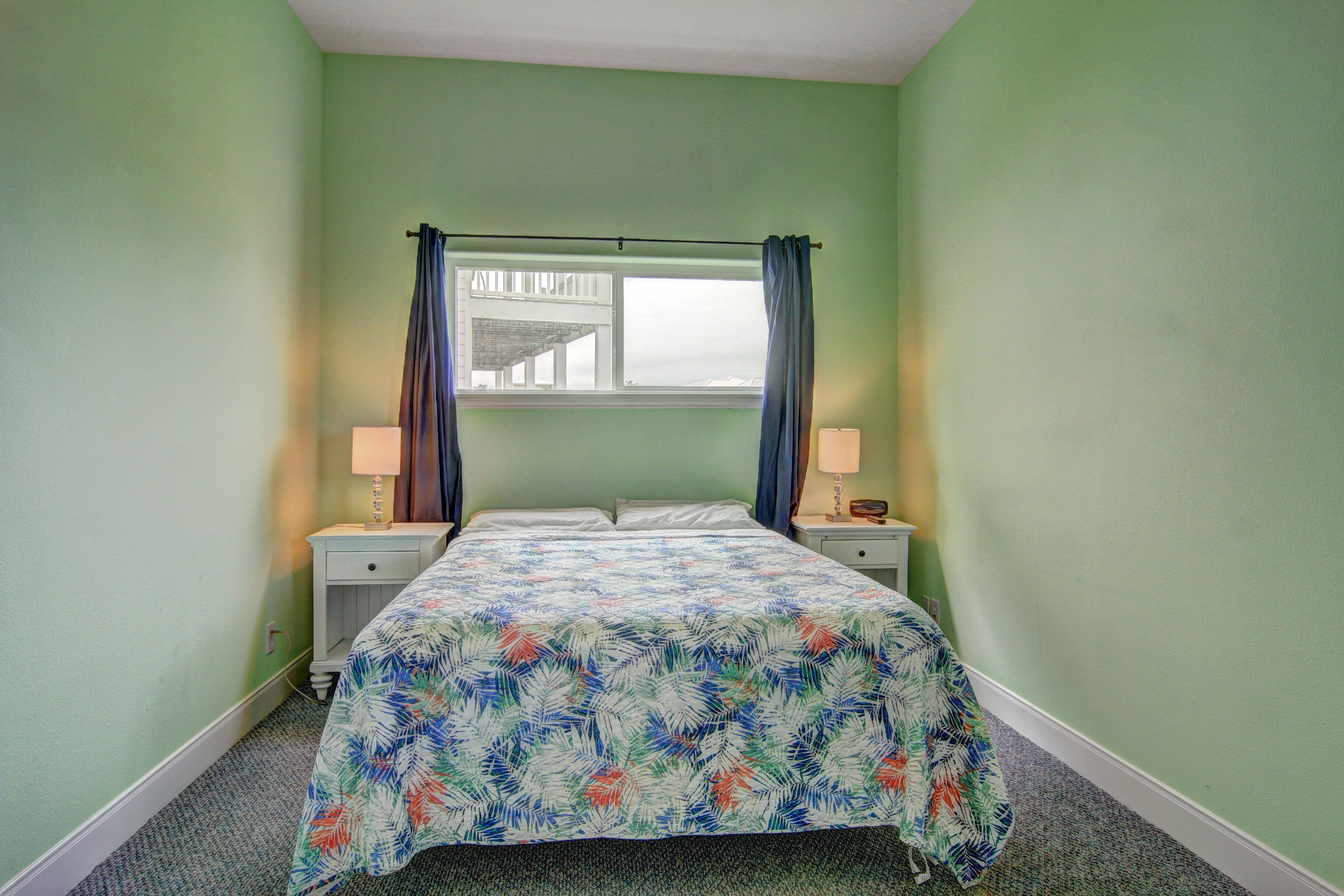 A bedroom with a bed, two bedside tables, a window with curtains, and a view of the outside.