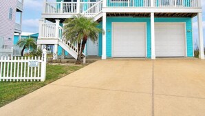 A two-story house with a balcony, a garage, and a white picket fence. - Casa Las Palmas - Pet Friendly! Boardwalk to the Beach! (Port Aransas)