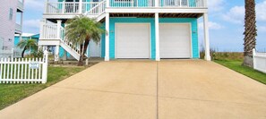 A two-story house with a balcony, a garage, and a white picket fence. - Casa Las Palmas - Pet Friendly! Boardwalk to the Beach! (Port Aransas)