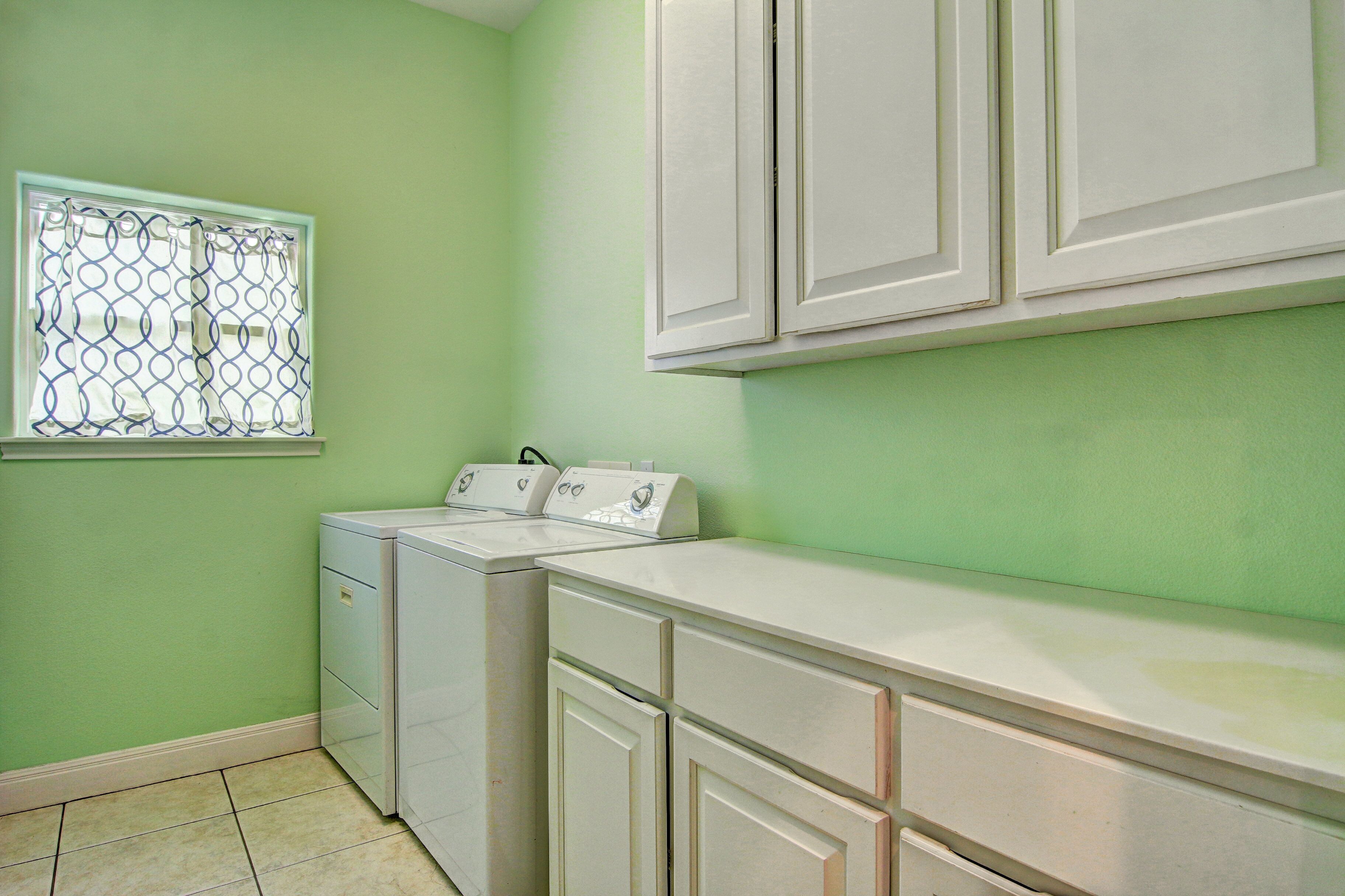 A laundry room with a washing machine and dryer, a window with a metal screen, and white cabinets.