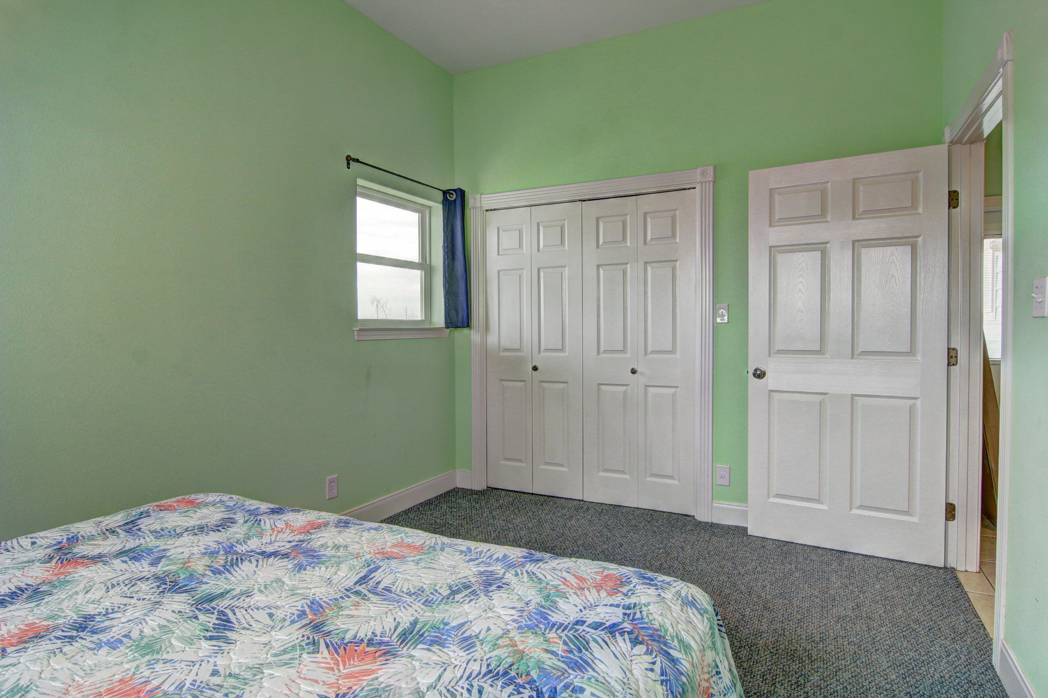 A bedroom with a bed, a window with a curtain, and a door.