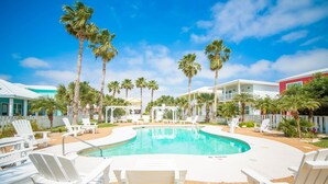 A pool area with white lounge chairs, palm trees, and a clear blue sky. - Casa Azul - Boardwalk to the Beach! (Port Aransas)