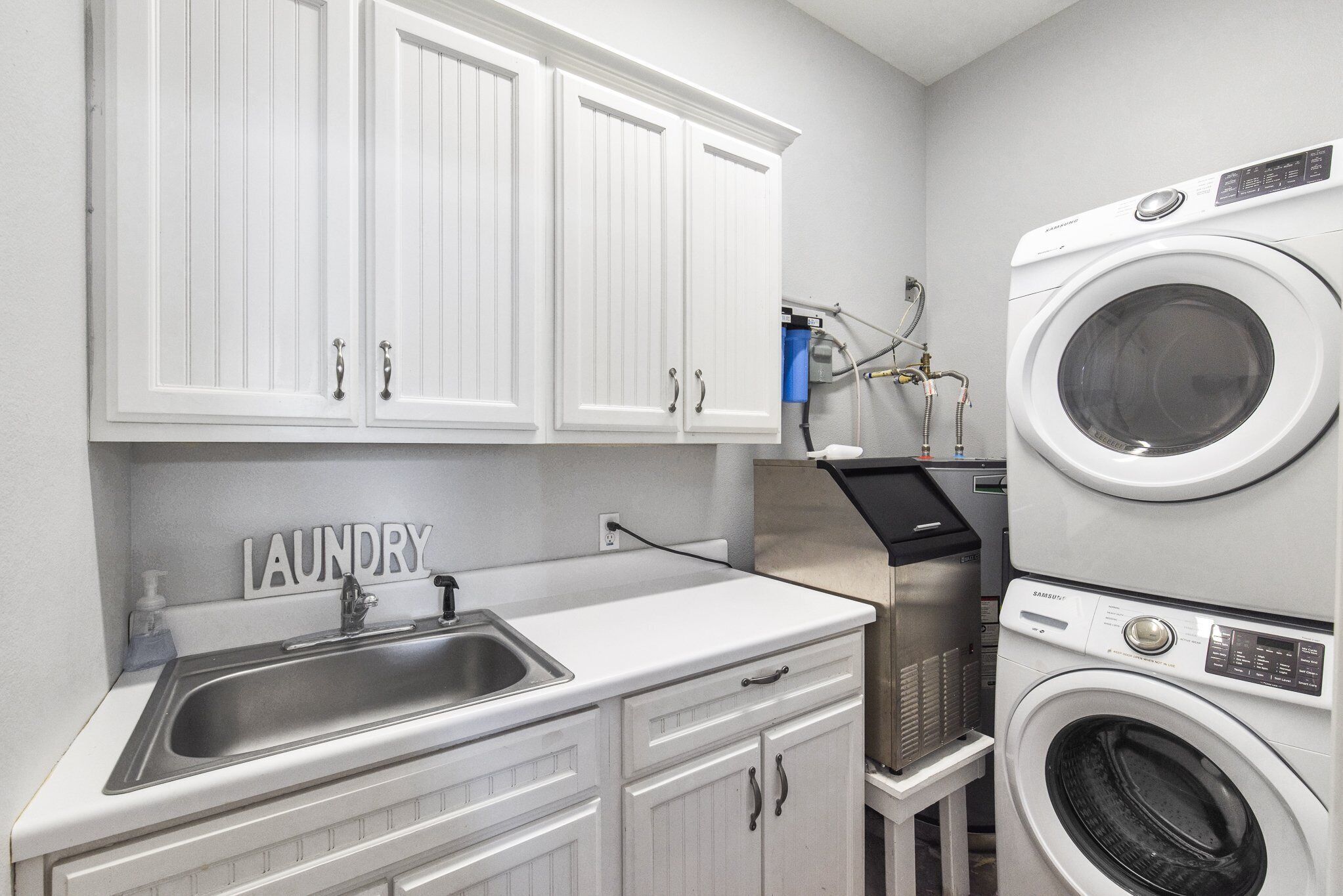 A laundry area with a sink, cabinets, and stacked washing machines.