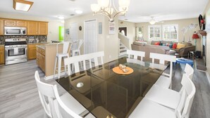 A modern kitchen with wooden cabinets, a microwave, and a dining area with a glass table and white chairs. - Palma Verde - Pet Friendly! (Port Aransas)