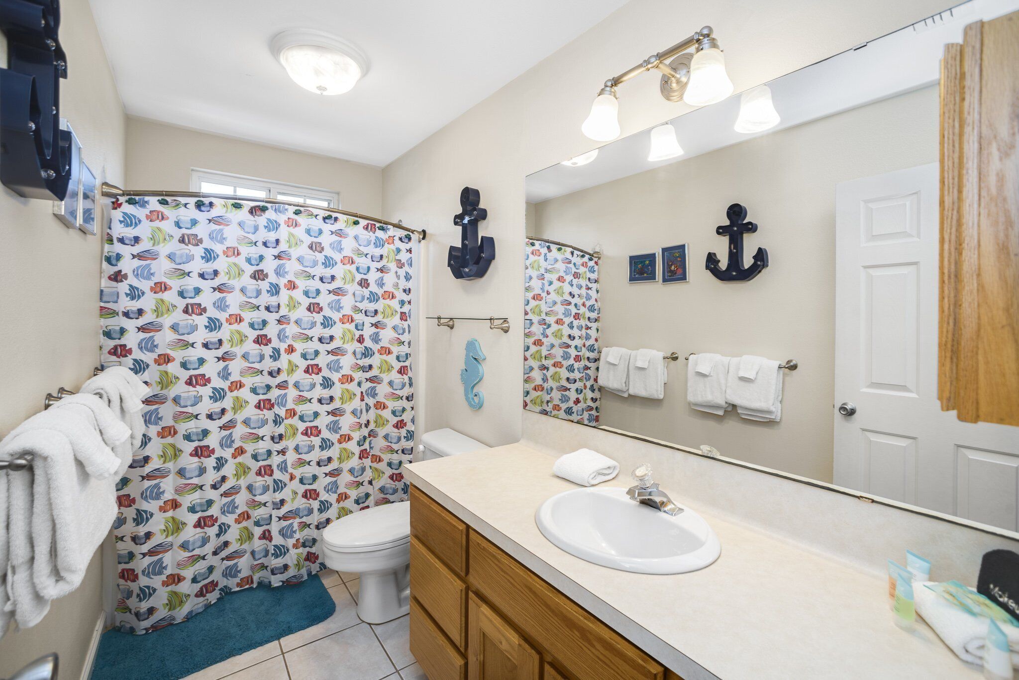 A bathroom with a shower curtain featuring a fish pattern, a white sink, wooden cabinets, and a large mirror.