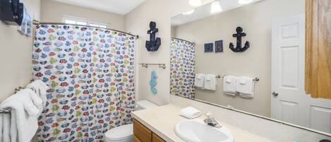 A bathroom with a shower curtain featuring a fish pattern, a white sink, wooden cabinets, and a large mirror.