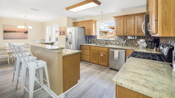 A modern kitchen with wooden cabinets, a stainless steel refrigerator, a gas stove, and a breakfast bar with bar stools. - Palma Verde - Pet Friendly! (Port Aransas)