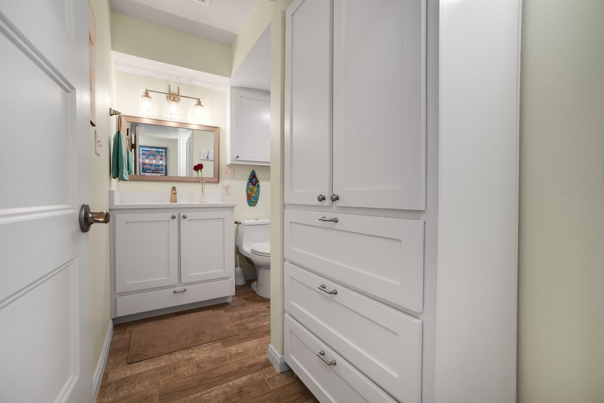 A bathroom with white cabinetry, a wooden floor, and a mirror with lights.