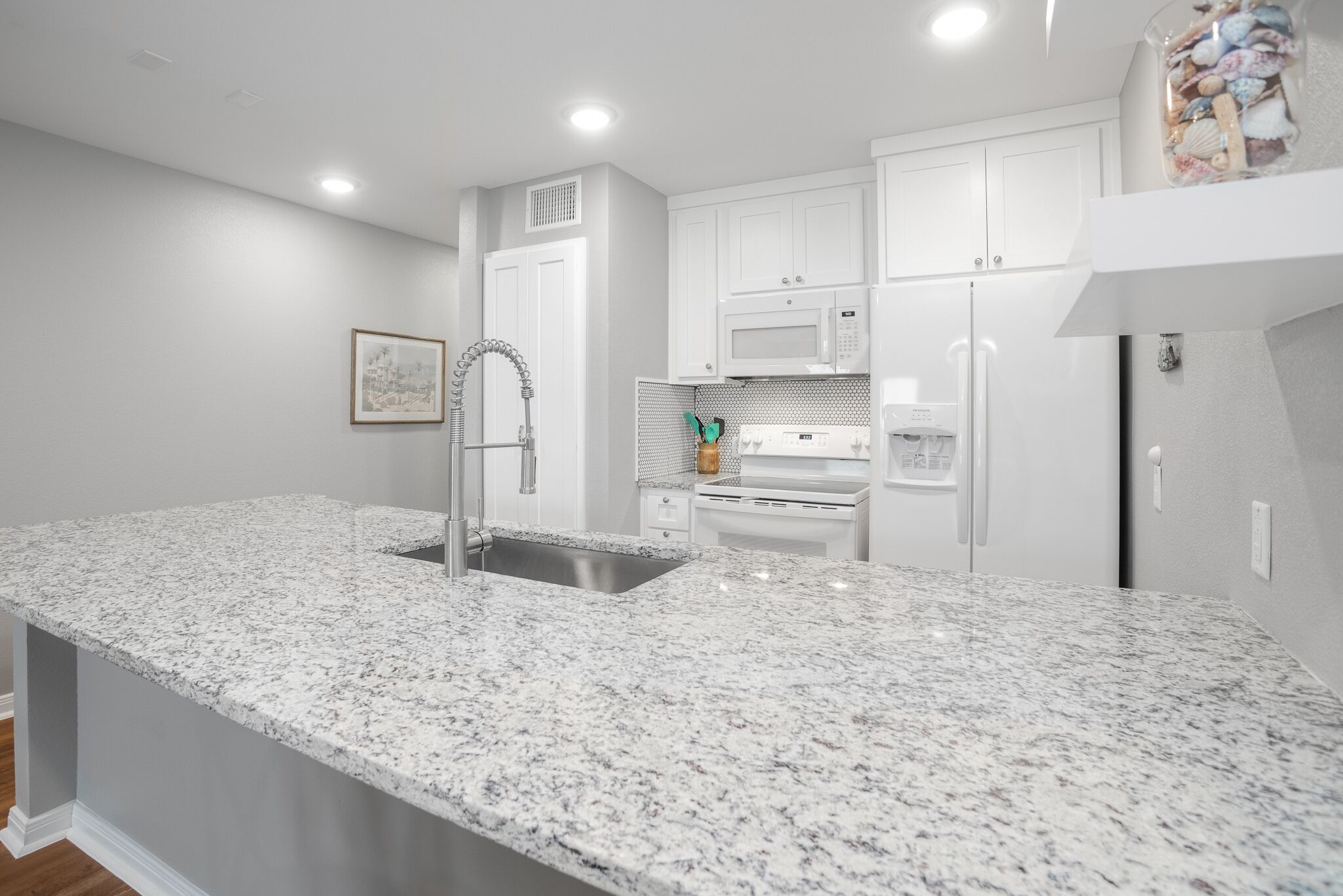 A kitchen with white cabinets, a granite countertop, stainless steel sink, and white appliances.