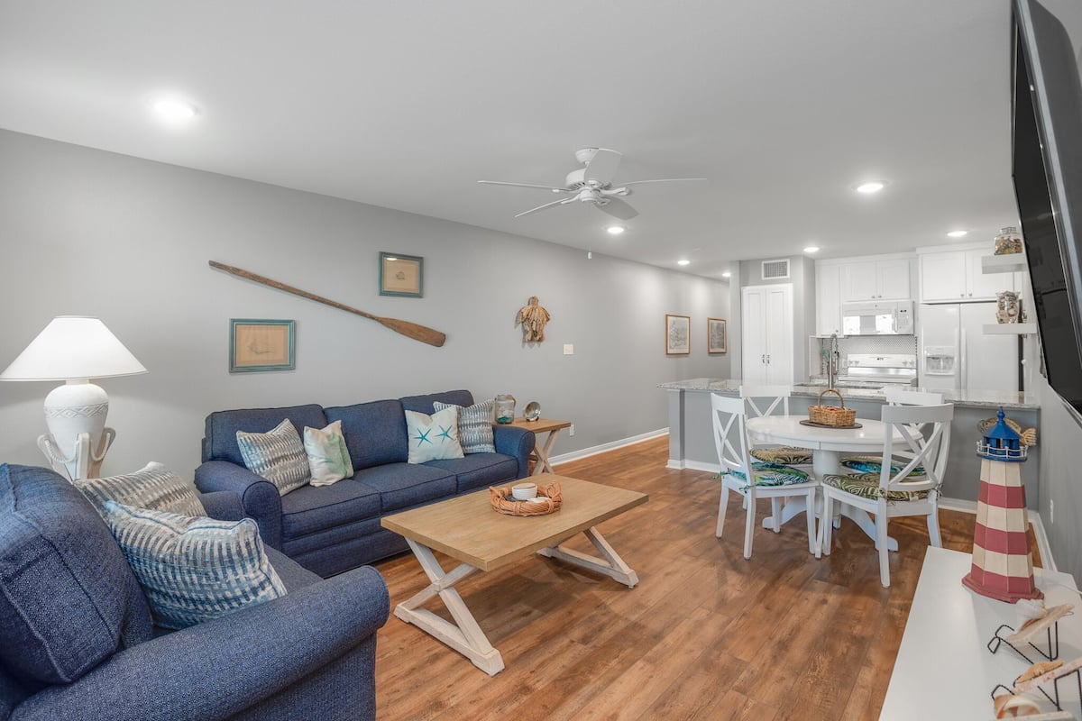 Un salon moderne avec un canapé bleu, une table basse en bois et un coin repas comprenant des chaises blanches et une petite table.