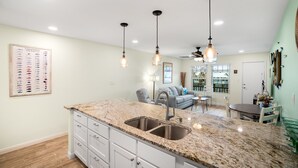 A kitchen with granite countertops, a double sink, pendant lighting, and a dining area with a table and chairs. - Sunrise Villas Condos (Port Aransas)