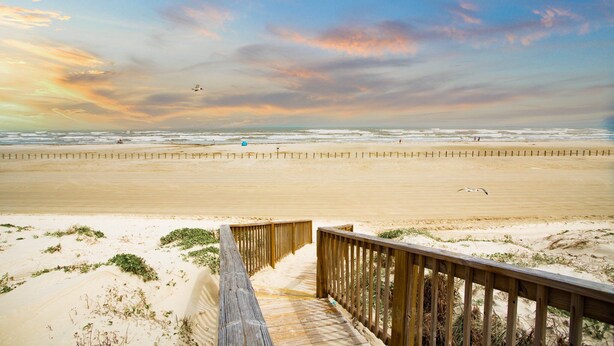 A wooden boardwalk leading to a beach with a clear sky and a few clouds. - Sunrise Villas Condos (Port Aransas)