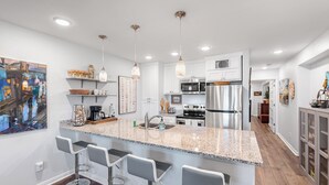 A modern kitchen with a granite countertop, stainless steel appliances, and bar stools. - Sunrise Villas Condos (Port Aransas)
