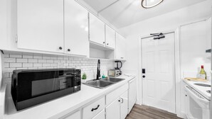 A modern kitchen with white cabinets, a black microwave, and a sink. - Stocked Condo - Sleeps 10 - Palmwavestays (Coconut Creek)