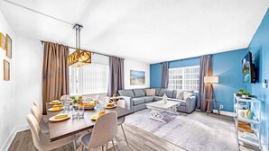 A modern living room with a dining area, a gray sectional sofa, a coffee table, and a TV on a stand. - Stocked Condo - Sleeps 10 - Palmwavestays (Coconut Creek)