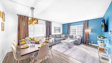 A modern living room with a dining area, a gray sectional sofa, a coffee table, and a TV on a stand.