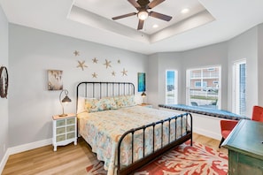 A bedroom with a bed, a nightstand, a desk, a chair, a ceiling fan, and a window with blinds. - Coconut Hut - Pet Friendly! Boardwalk to the Beach! - Pet Friendly! Boardwalk to the Beach! (Port Aransas)