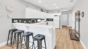 A modern kitchen with white cabinets, a central island with stools, and a backsplash with green tiles.