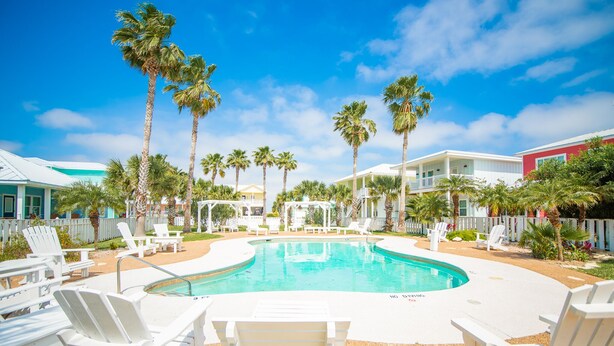 A pool area with white lounge chairs, palm trees, and a clear blue sky.