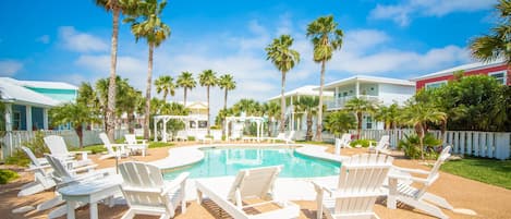 Un espace piscine avec des chaises longues blanches et des palmiers.