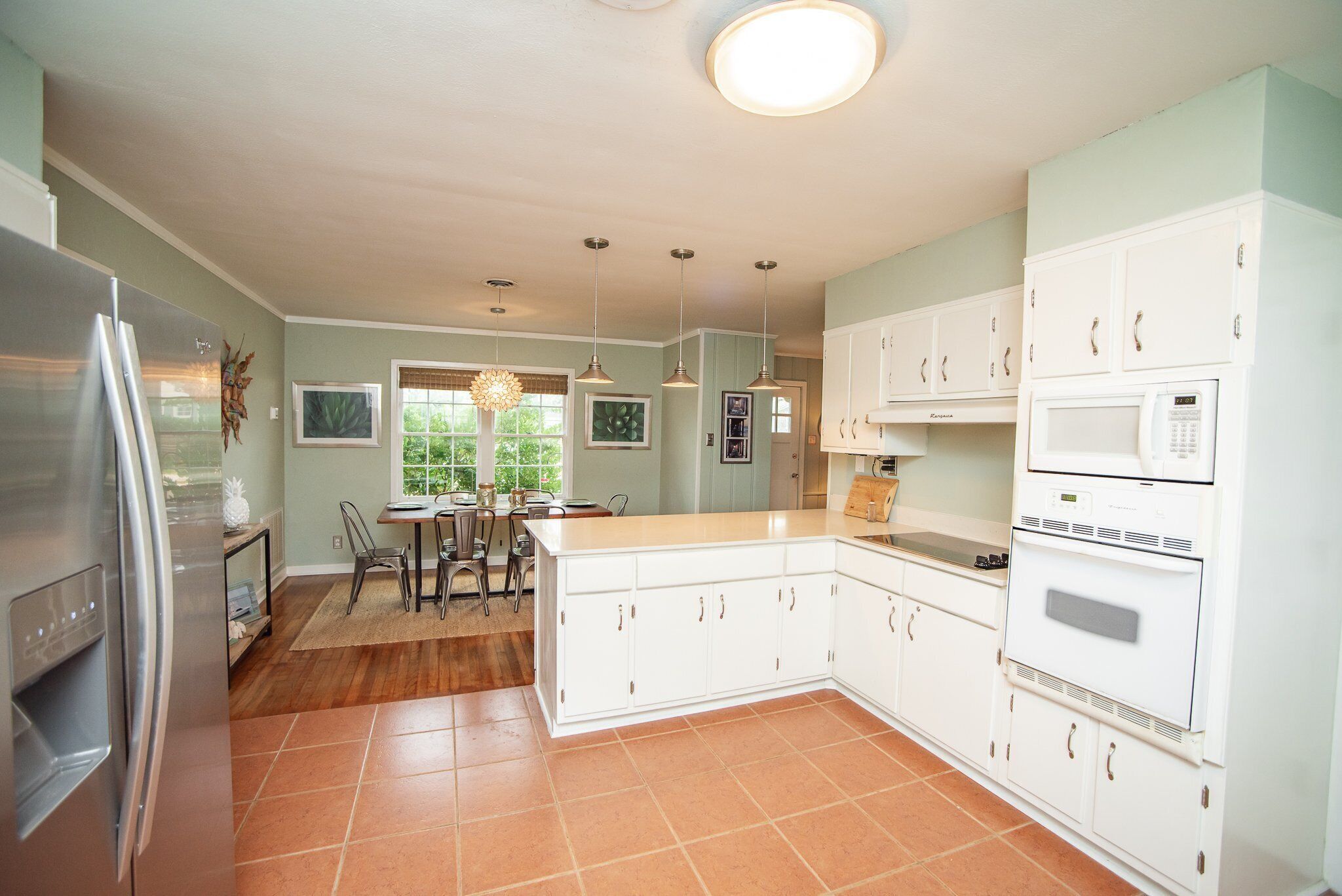 A kitchen with white cabinets, a stainless steel refrigerator, a built-in oven, and a dining area with a table and chairs.