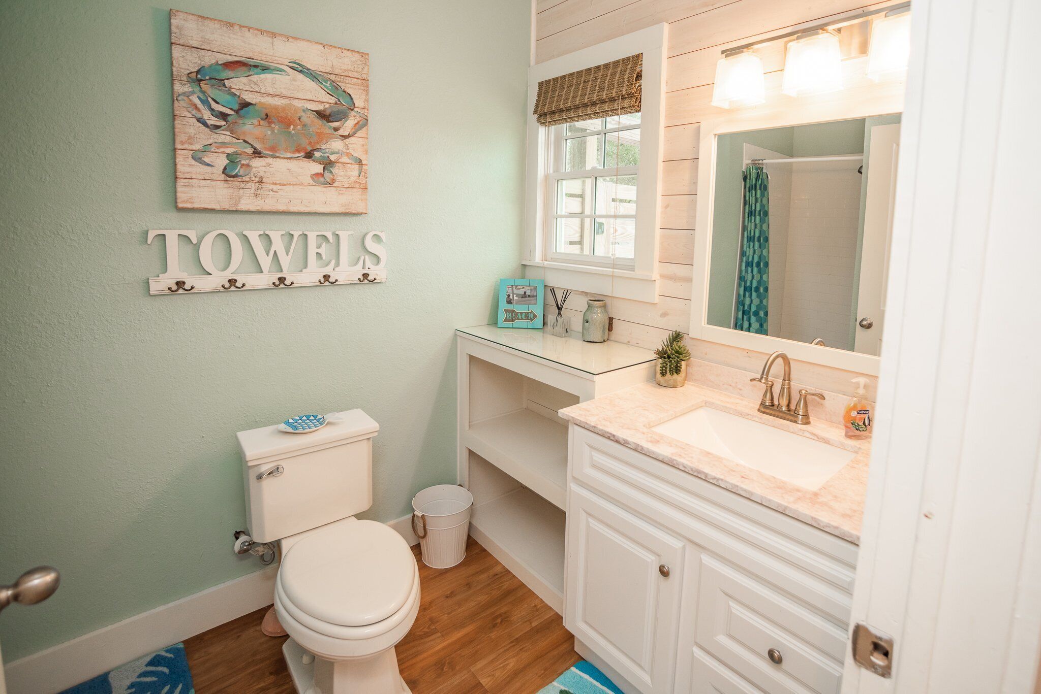 A bathroom with a toilet, sink, and mirror. There is a towel rack above the toilet and a sign that reads "TOWELS".