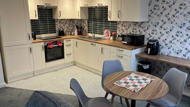 A compact kitchen with white cabinets, a microwave, a kettle, and a coffee maker. There is a dining area with a table and chairs. - Sleeps 4 With Ensuite and Free Parking (Lincoln)
