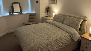 A bedroom with a large bed, a bedside table with a lamp, a chair, a window with a picture frame, and a wall decoration. - Sleeps 4 With Ensuite and Free Parking (Lincoln)