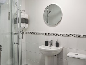 A bathroom with a glass shower enclosure, a white sink with a black soap dispenser, a toilet, and a mirror on the wall. - Hogarth Apartment by the Sea-UK46447 (Newbiggin-by-the-Sea)