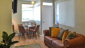 Ein Wohnzimmer mit braunem Ledersofa, einem Esstisch mit Stühlen, einer Hängelampe und einem großen Fenster.