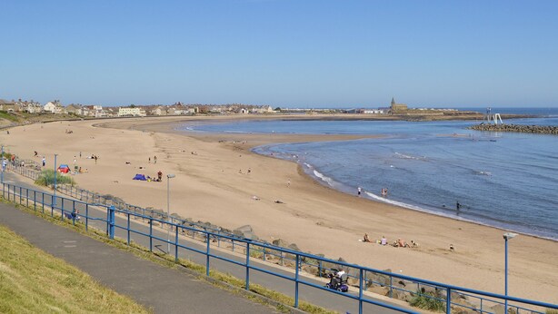 Ein Strand mit blauem Himmel, sandigem Ufer und einigen Personen.