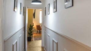 Ein Flur mit gerahmten Bildern an der Wand, einem Blumentopf und einem Essbereich im Hintergrund.