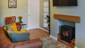 Ein Wohnzimmer mit braunem Ledersofa, einem an der Wand montierten Fernseher, einem Kamin und einer Tür.