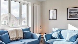 Une pièce avec deux canapés bleus, un radiateur blanc, un tableau encadré au mur et une fenêtre donnant sur des immeubles.