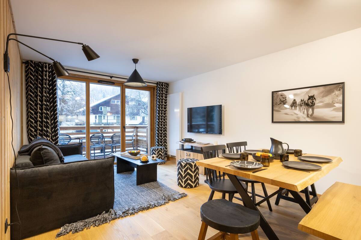 Ein modernes Wohnzimmer mit einer Couch, einem Esstisch mit Stühlen, einem Couchtisch und einem Fernseher an der Wand.