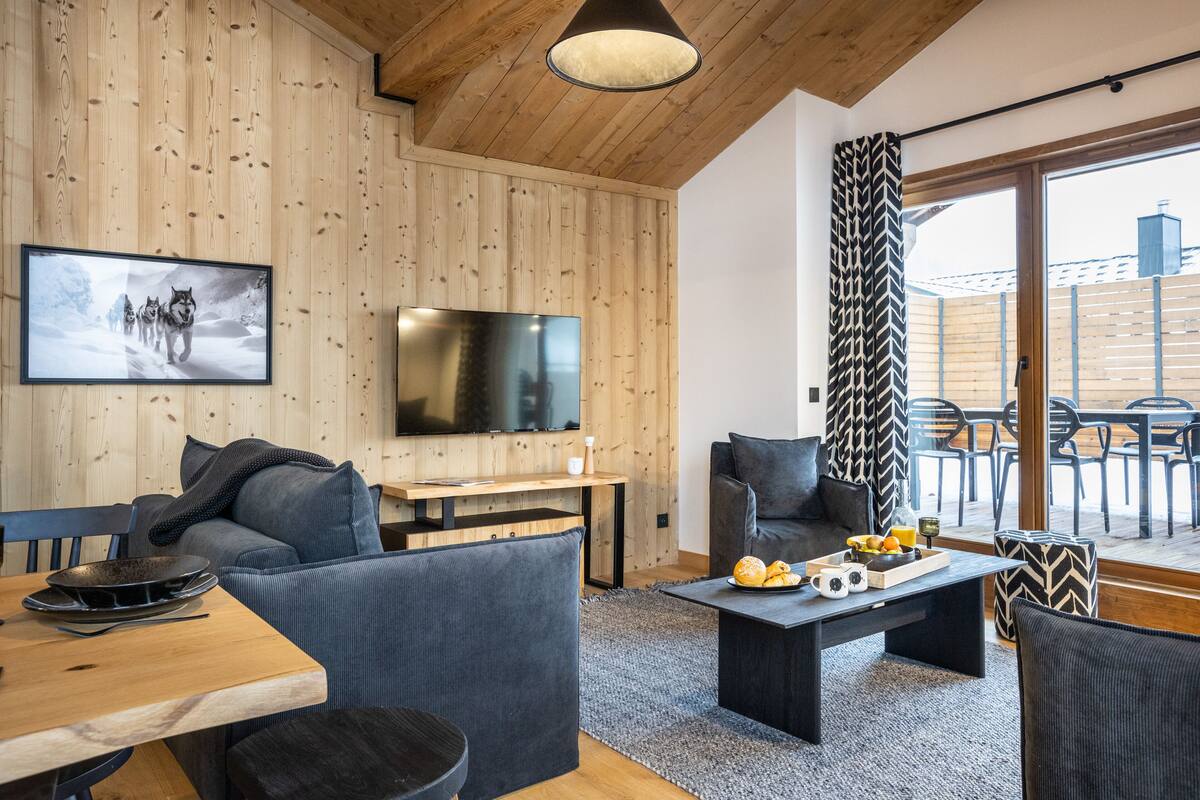 Ein modernes Wohnzimmer mit Holzverkleidung, einem Flachbildfernseher, einem Sofa, einem Couchtisch und einem Essbereich mit Holztisch und Stühlen.