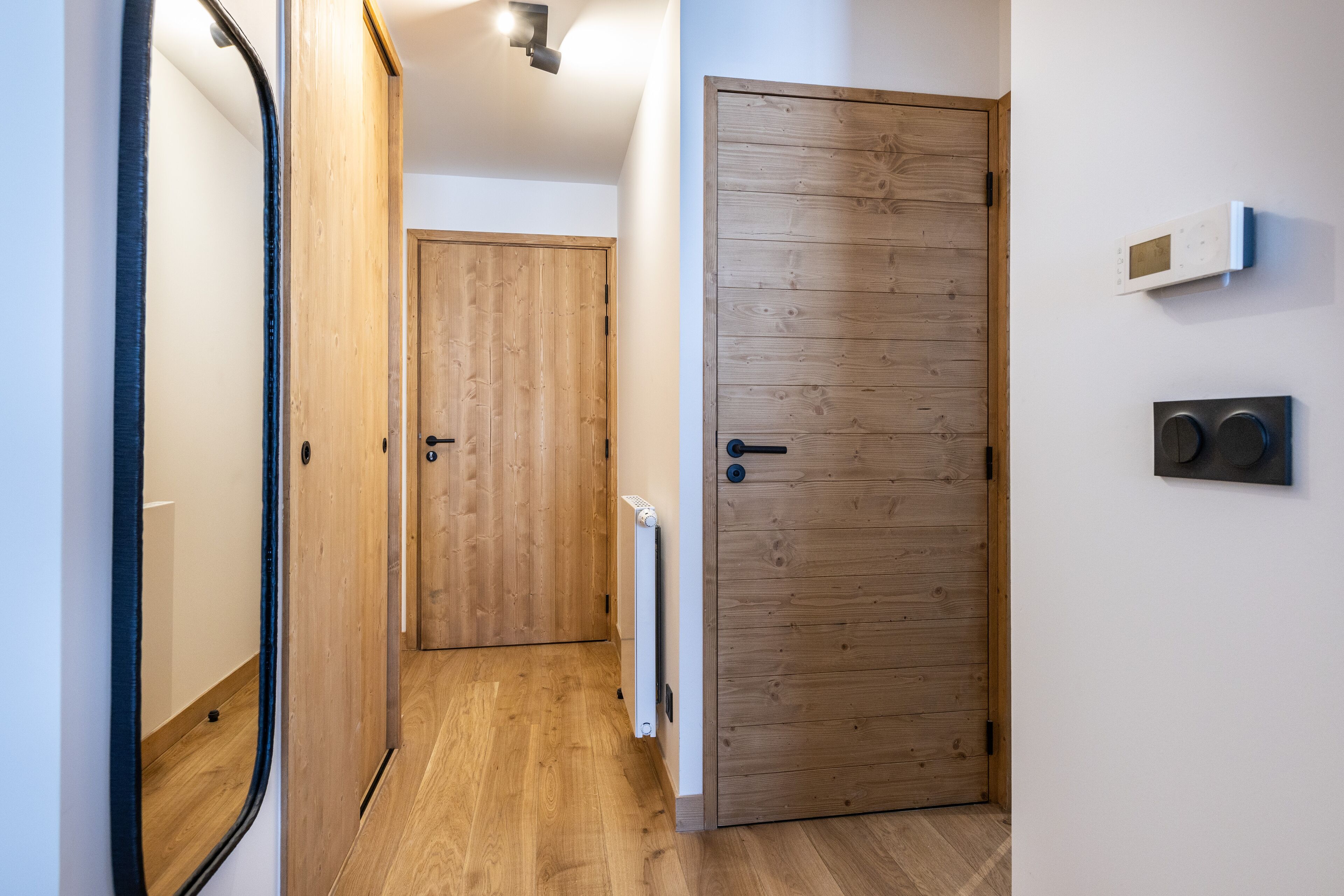 Ein Korridor mit Holztüren, einem Heizkörper und einem Thermostat an der Wand.