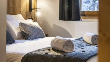 Une chambre à coucher avec un lit, une lampe fixée au mur, une fenêtre avec des rideaux et une vue sur les arbres à l’extérieur.