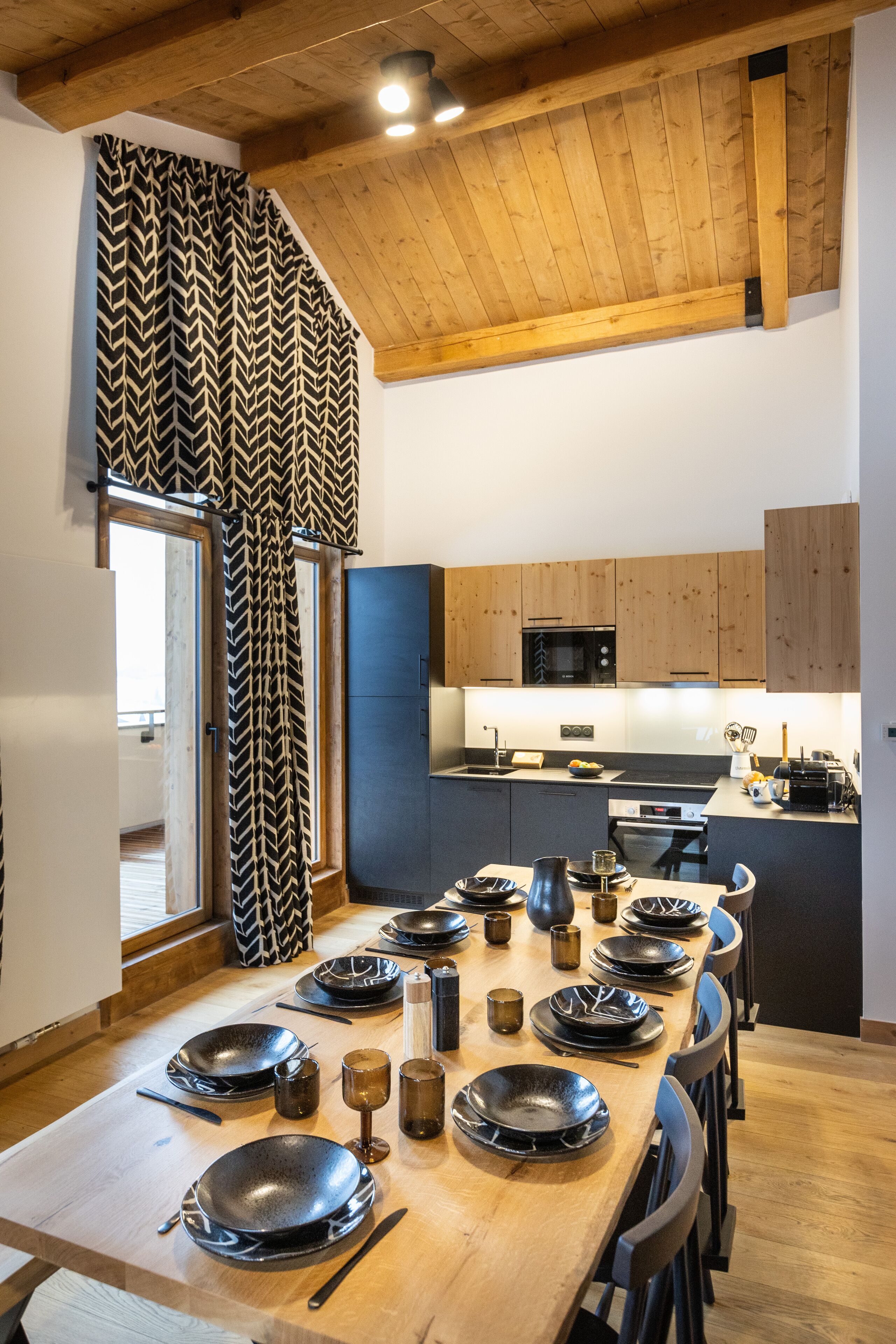 Una cocina moderna con armarios de madera, una mesa de comedor preparada para seis comensales y vistas del área de estar contigua.
