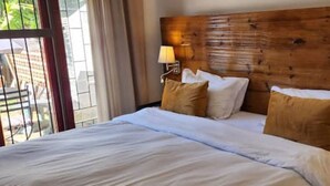 Een hotelkamer met een houten hoofdeinde, twee bedden met witte lakens en twee bedlampen.